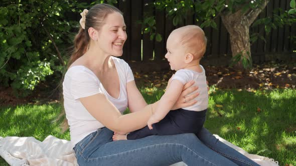 Happy Smiling Mother Sitting on Blanket at Garden and Playing with Her Little Baby Son