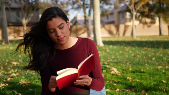 A young woman college literature student studying and reading a book on a campus lawn or outdoor par