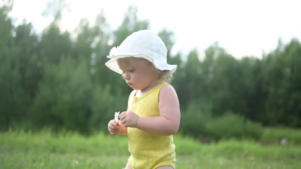 Little Funny Cute Blonde Girl Child Toddler in Yellow Bodysuit and White Hat Walking in Field with