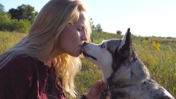 Close Up of Young Girl with Blonde Hair Holding a Piece of Chocolate in Her Mouth and Siberian Husky