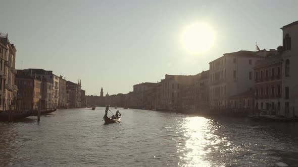 Gondola sailing in Canal Grande lit by warm sunrise with water reflections, Venice, Italy