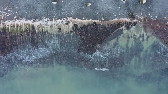 Descending top down aerial shot of blue water waves crashing on wild rugged beach