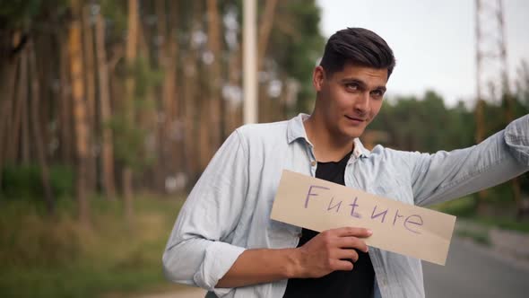 Handsome Young Positive Man Hitchhiking with Future Banner on Suburban Road at Forest