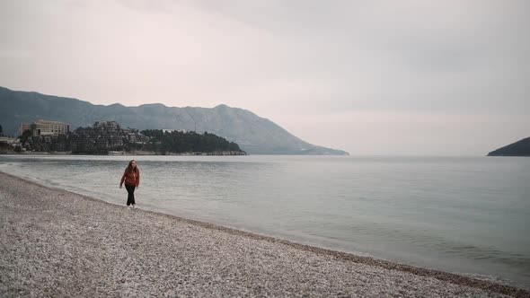 Lonely Young woman walks along the sea in spring cloudy weather