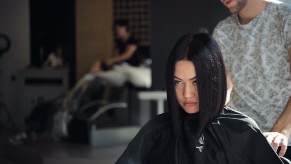 Young Professional Hip Male Hairdresser Cutting Dark Hair of Client Woman at Salon