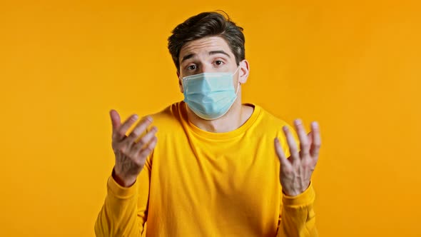 Young Handsome Unsure Guy in Sterile Mask Shrugs His Arms, Makes Gesture of I Don't Know, Can't Help