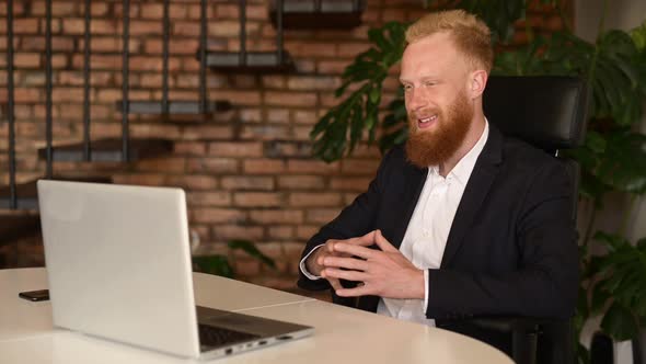 Positive Redhead Bearded Businessman in Formal Suit Making Video Call on the Laptop