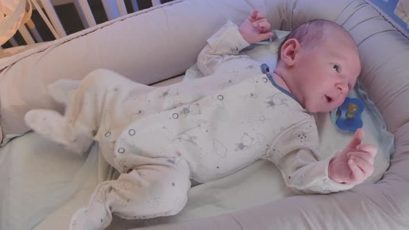 A newborn baby, one month old, rests restlessly in the crib