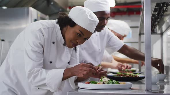 Diverse group of chefs garnishing dishes and similing in restaurant kitchen