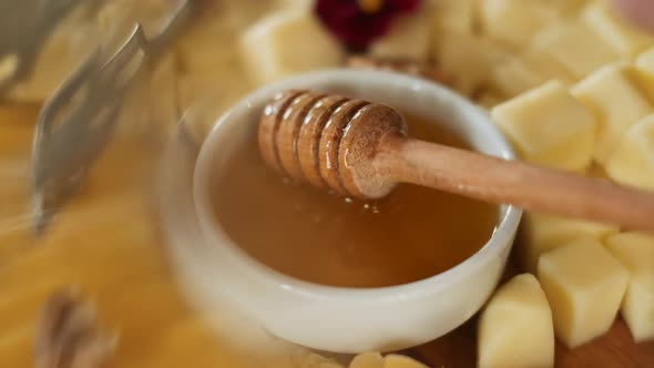 Sweet Honey On Wooden Plate With Different Cheeses, Flowers And Nuts.