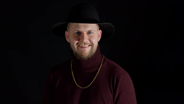 Portrait of Seductive Smiling Young Man in Trendy Stylish Clothes and Hat Against Black Background