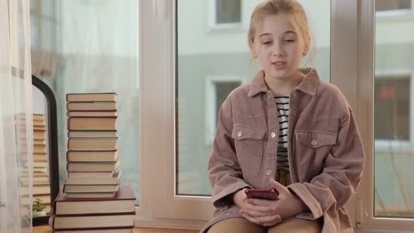 Girl Sitting on the Windowsill and Looking at the Phone