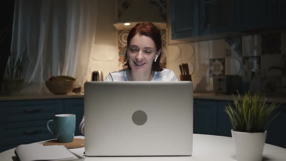 Woman In The Kitchen With Laptop, Woman Smiling. She Communicates With Someone Through Laptop