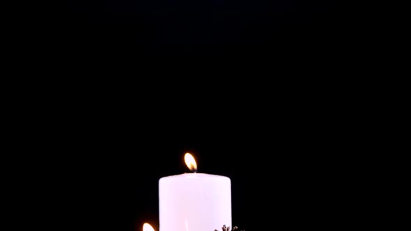 Burning candles and pine cones against black background