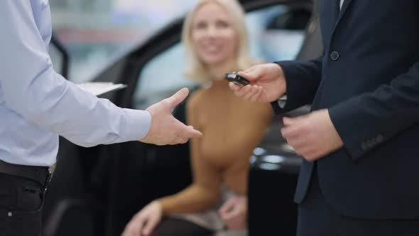 Unrecognizable Men Passing Car Key and Shaking Hands with Blurred Woman Smiling at Background