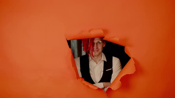 Well Dressed Man with Bright Hairstyle Looking Out Out of Hole of Orange Background