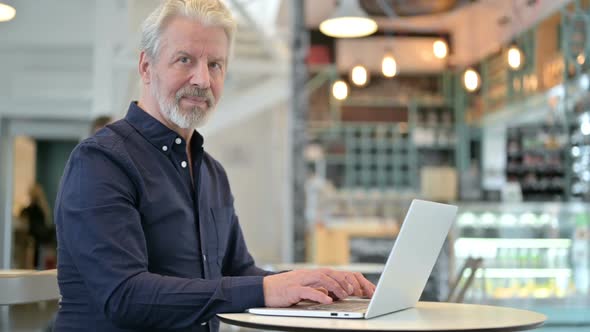 Old Man with Laptop Smiling at Camera in Cafe