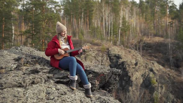 Caucasian Woman Sits on Rock and Plays the Ukulele