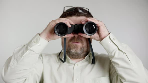 Middle aged man in green shirt looks ahead through binoculars.