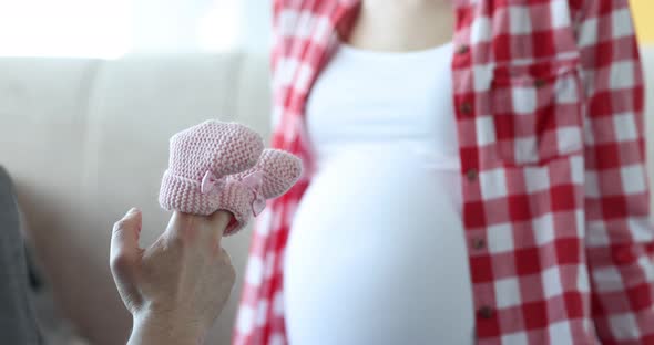 Man Holds Pink Baby Slippers Next to Pregnant Woman