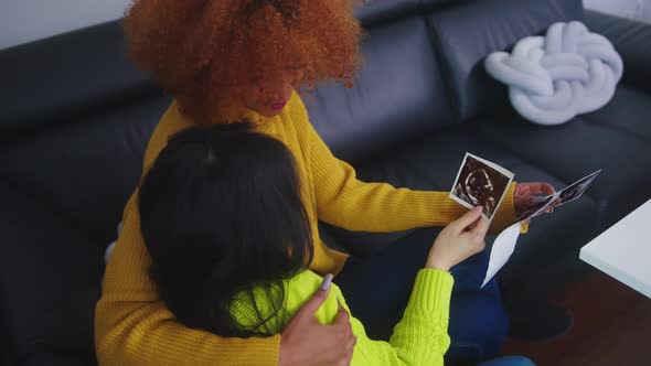 Lesbians Waiting for Baby Embracing and Looking at Ultrasound Picture. 