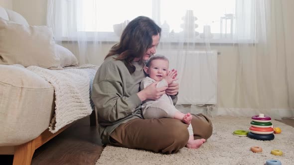 A happy child plays patties with his mother on the carpet in the home room. Toddler baby boy smiles