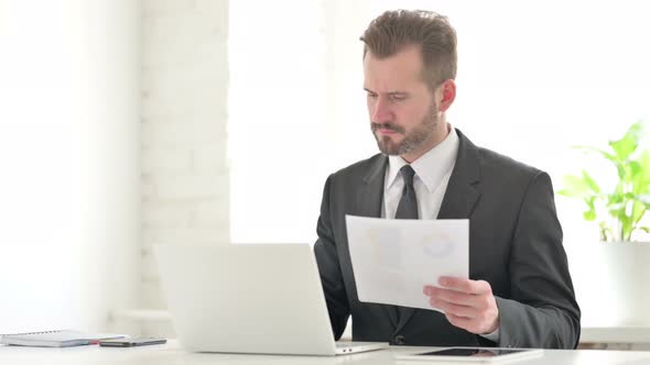 Young Businessman with Laptop Celebrating Success While Reading Documents