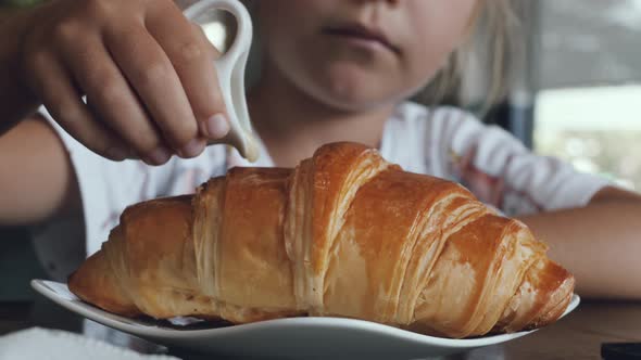 Girl pours condensed milk on a croissant