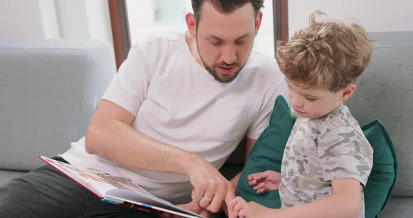 Close Up of Father and Son are Spending Time Together at Home By Reading a Book on the Sofa and