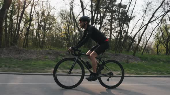 Cyclist wearing black jersey and shorts riding a black professional road bike in the park