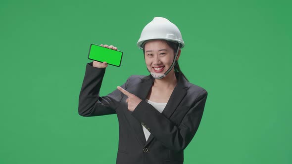 Smiling Asian Female Engineer Pointing To Green Screen Smartphone In The Green Screen Studio