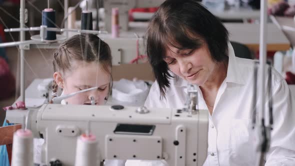 Grandma with Little Granddaughter Sew Clothes in the Factory