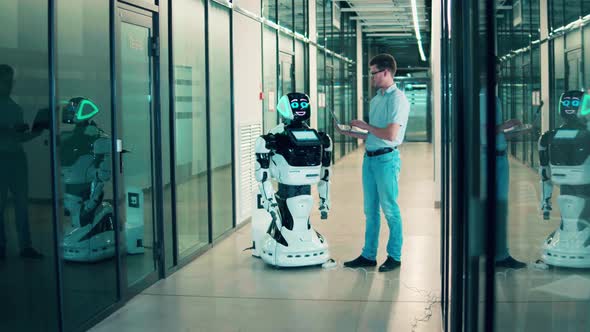 Male Engineer with a Laptop Is Managing a Robotlike Machine