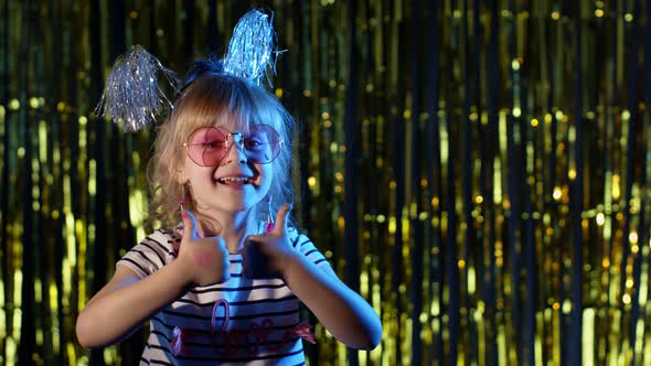 Trendy Girl in Stylish Glasses Standing on Blue Neon Lights Pointing at Blank Space Agree Sign