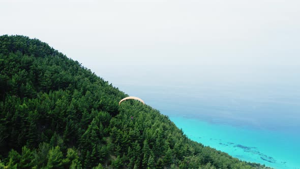 Drone view of paragliding over scenic hill and coastline.