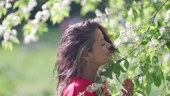 Pretty Woman is Playing with Blooming Branches of Tree in Garden in Spring