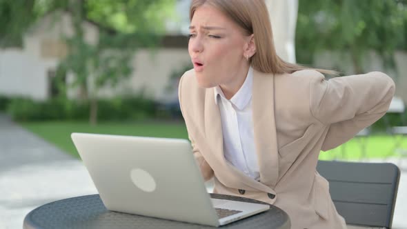 Young Businesswoman with Laptop Having Back Pain in Outdoor Cafe