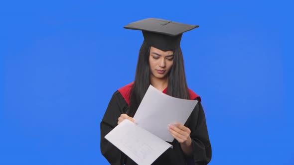 Portrait of Female Student in Graduation Costume Looking Through Documents Tearing Them Up and