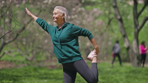 Happy Senior Sportswoman Standing on One Leg Stretching Muscles Outdoors