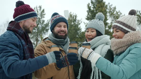 Cheerful Girls and Guys Enjoying Winter Day Outdoors Clinking Coffee Cups Laughing in Park