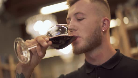 Portrait of Handsome Male Drinking Wine in the Liquor Store. Man Enjoys Wine Glass