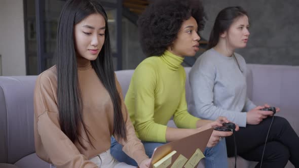 Irritated Young Asian Woman Rolling Eyes Looking Back at Relaxed Roommates Gaming Online