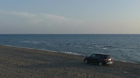 Aerial View of a Car Moving Along a Sandy Beach Along the Sea