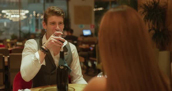 Happy Young Man Checks a Glass of Wine with a Woman Having Dinner at a Restaurant