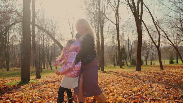 Mother circles daughter on arms at autumn park. Two females having fun. Girls spending time together