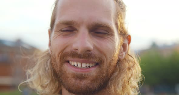 Bokeh Shot of Bearded Caucasian Young Man Smiling at Camera Outdoors