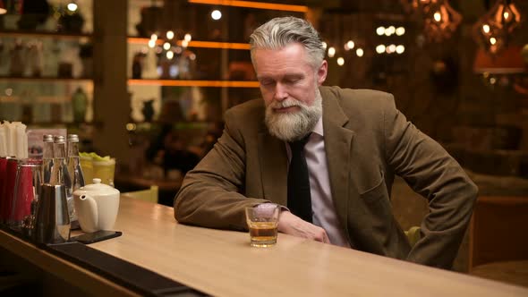 Lonely gray-haired man drinking whiskey at a bar