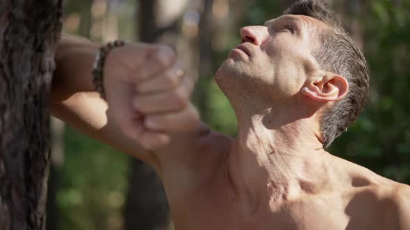 Closeup Portrait of Caucasian Topless Man Leaning on Tree Trunk in Sunlight Thinking