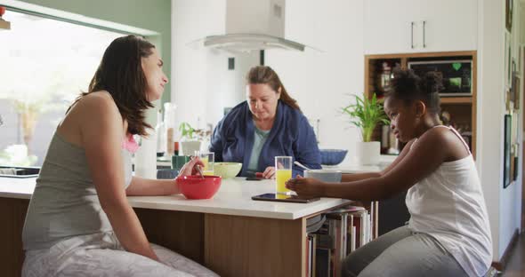 Happy caucasian lesbian couple and their african american daughter eating breakfast in kitchen