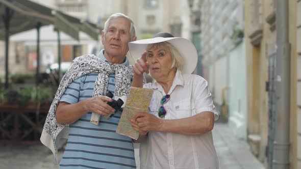 Senior Male Tourist Asking Woman for Directions in Town Using a Map in Hands